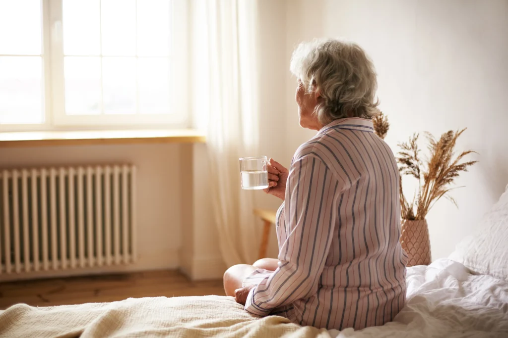 rear view senior sixty year old woman with gray hair holding mug washing down sleeping pill suffering from insomnia elderly retired female taking medicine with water sitting bedroom 1024x683 1